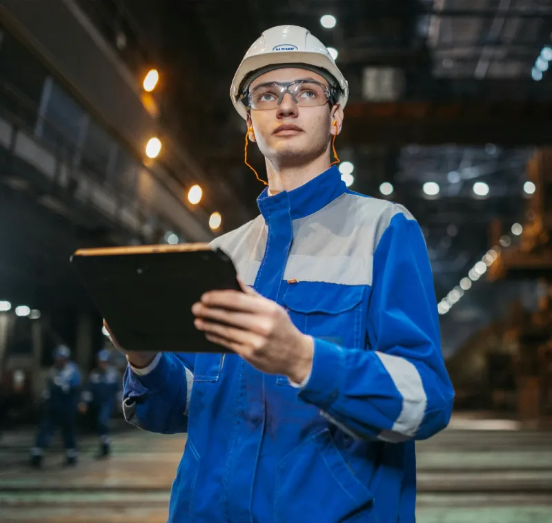 Medewerker op de werkvloer met helm op en tablet in hand